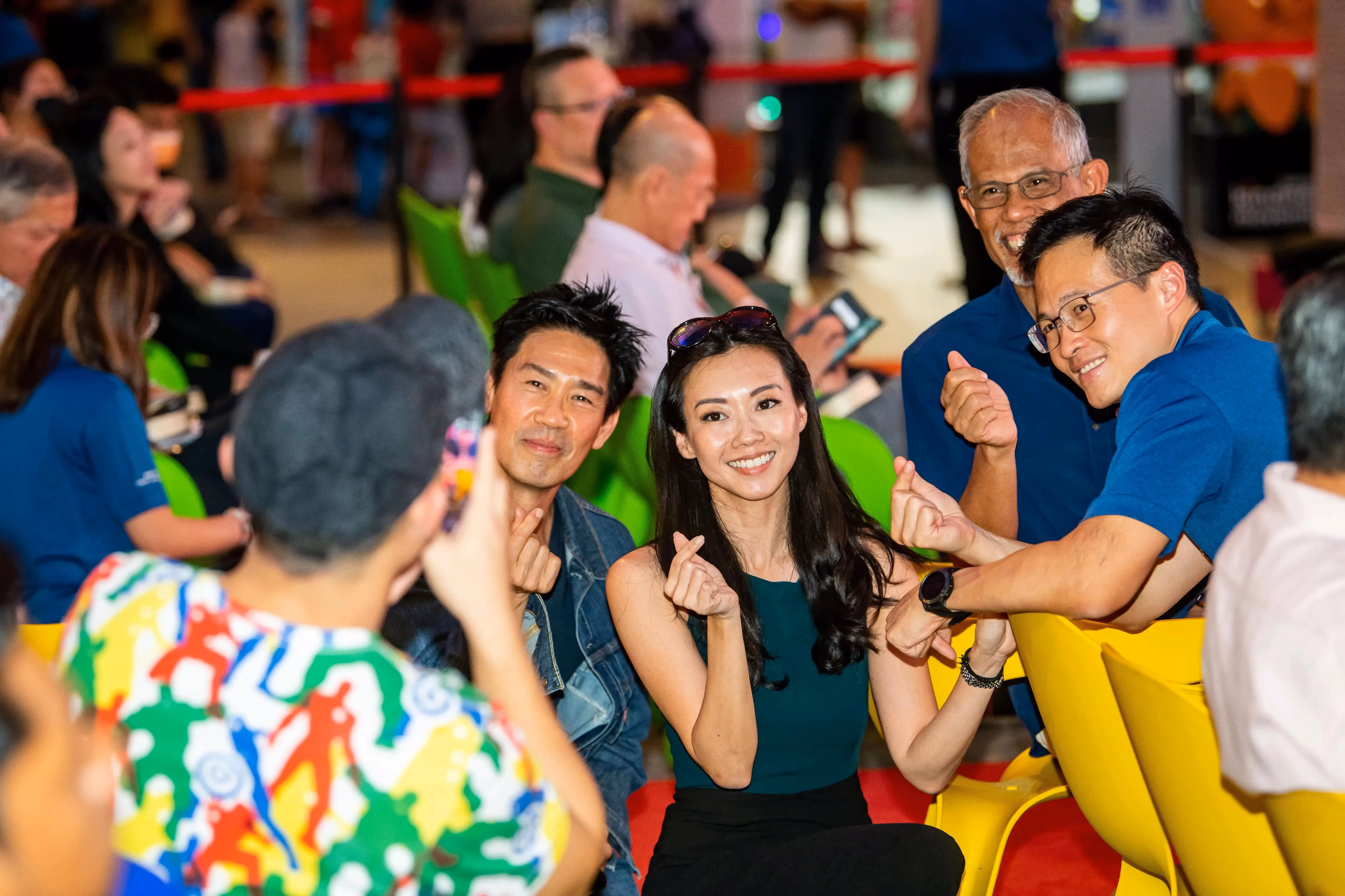 Several people are seated in bright-colored chairs, with one wearing a multicoloured shirt and taking a photo.